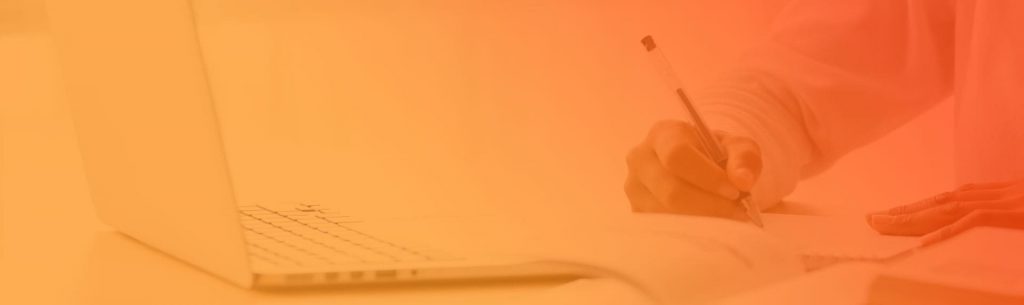 Person writing with pen and on paper sitting near laptop with orange gradient.