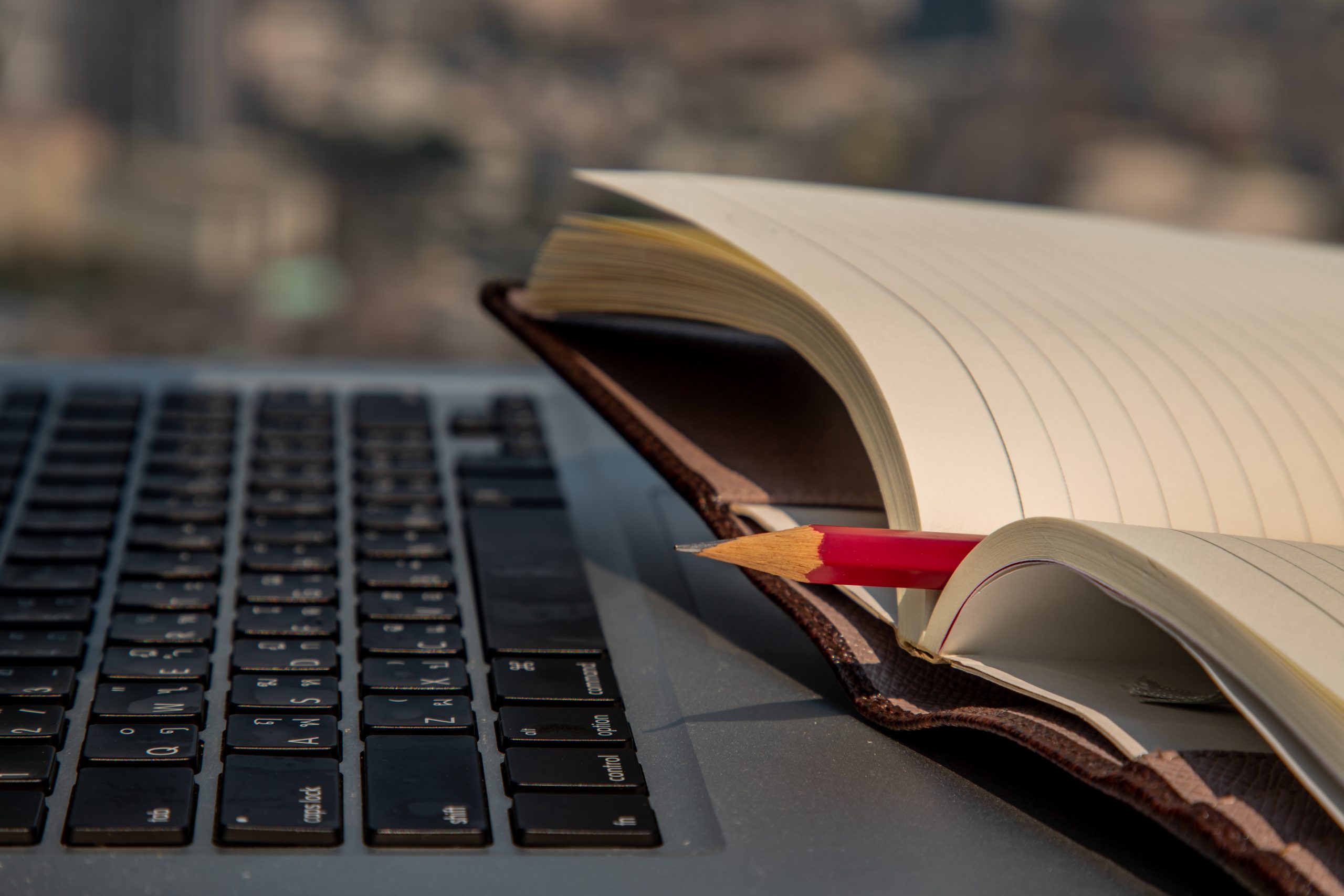 Close up of laptop on tale with open notebook and pen on top.