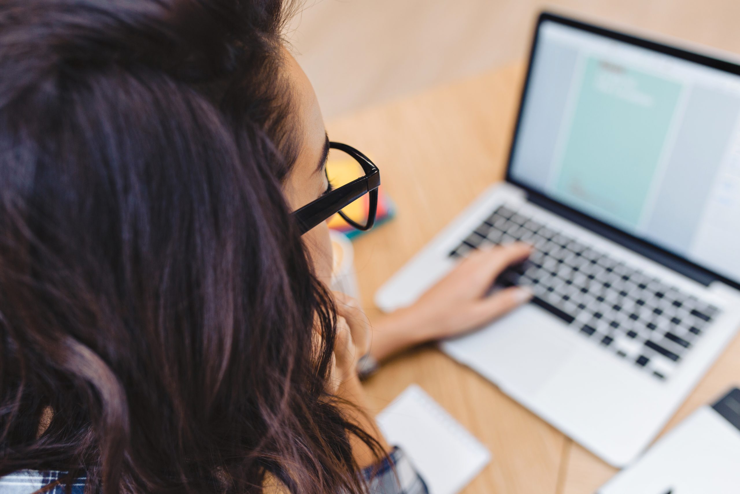 Closeup portrait from back brunette young woman in black glasses working with laptop on table. Surfing in internet, clever student, freelancer, working, searching, designing