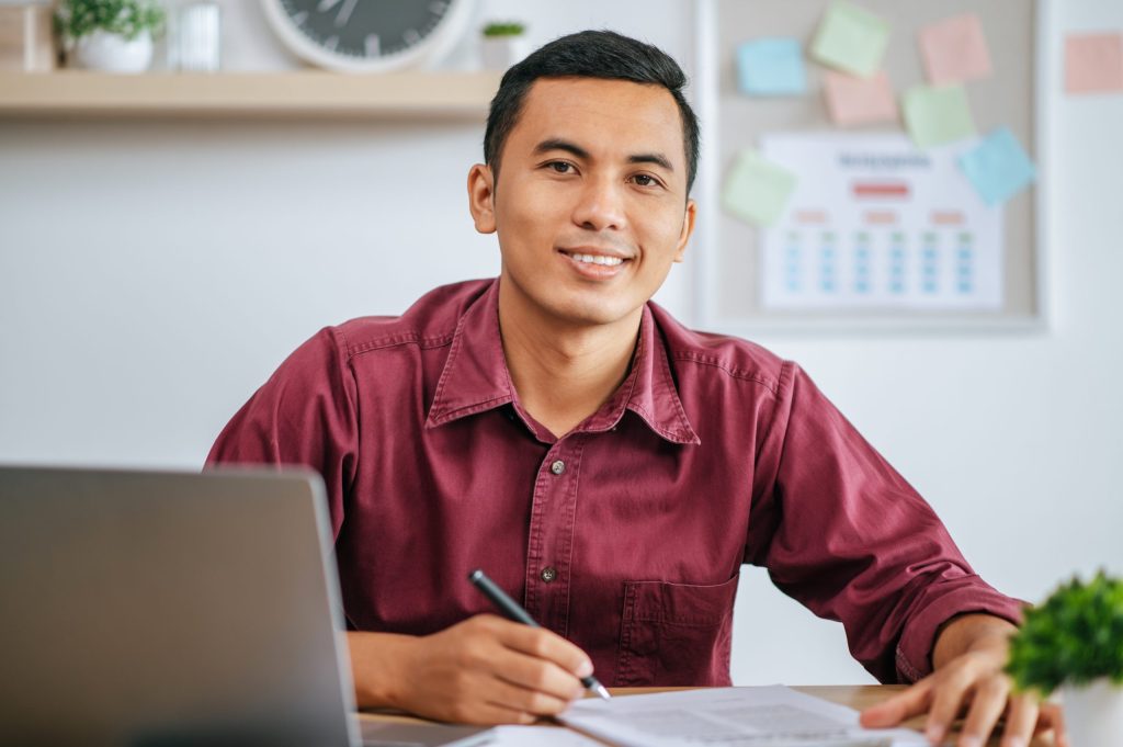 Male student smiling at camera working on laptop.
