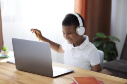 Young boy wearing headphones and working on a laptop at a desk.