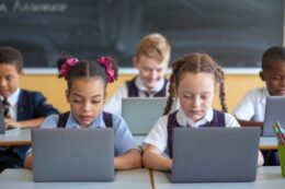 multiple students in classroom sitting at desks working on laptops