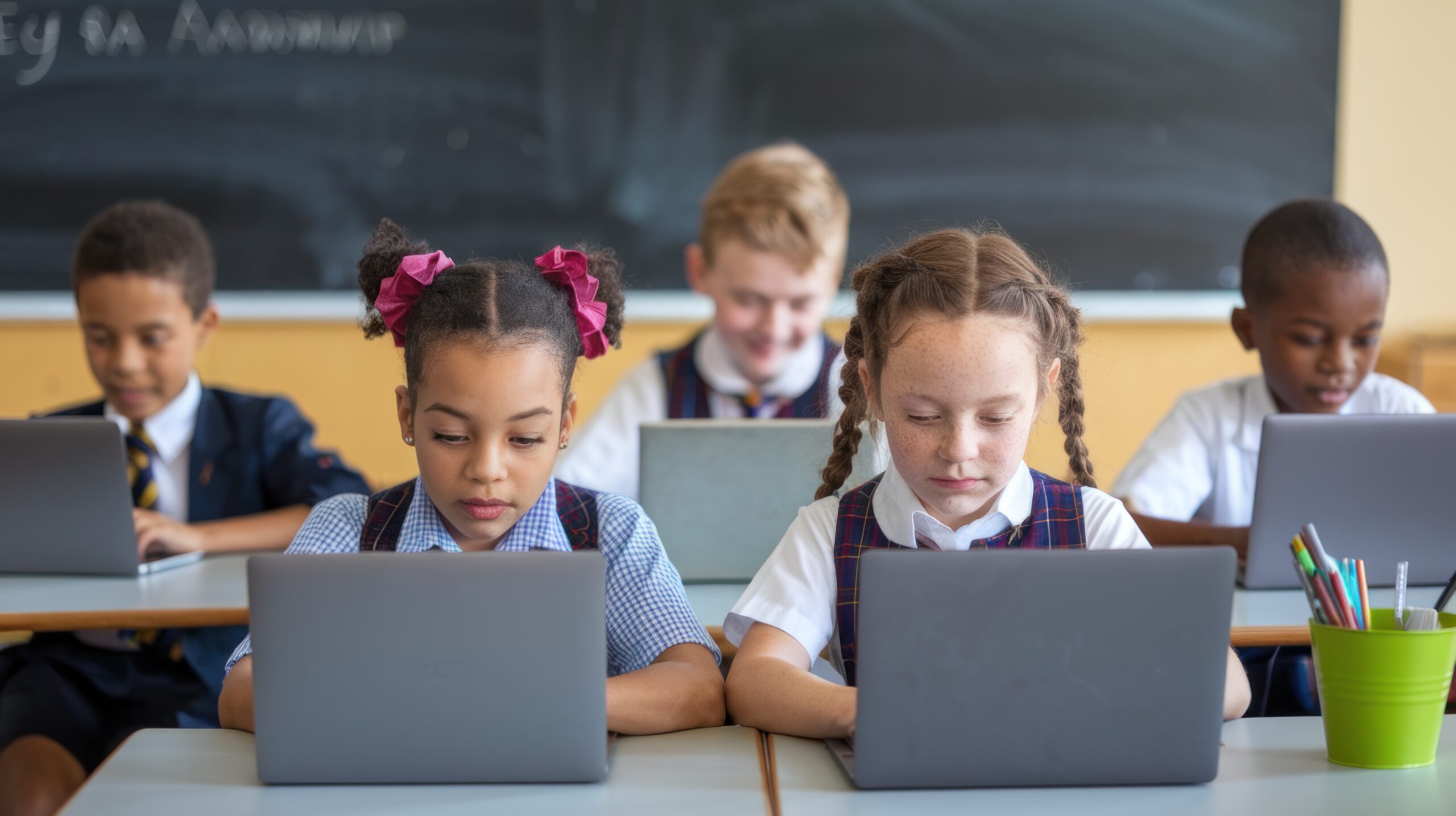 multiple students in classroom sitting at desks working on laptops