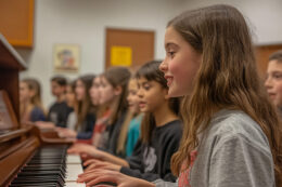 Students in classroom with girl student playing the piano.